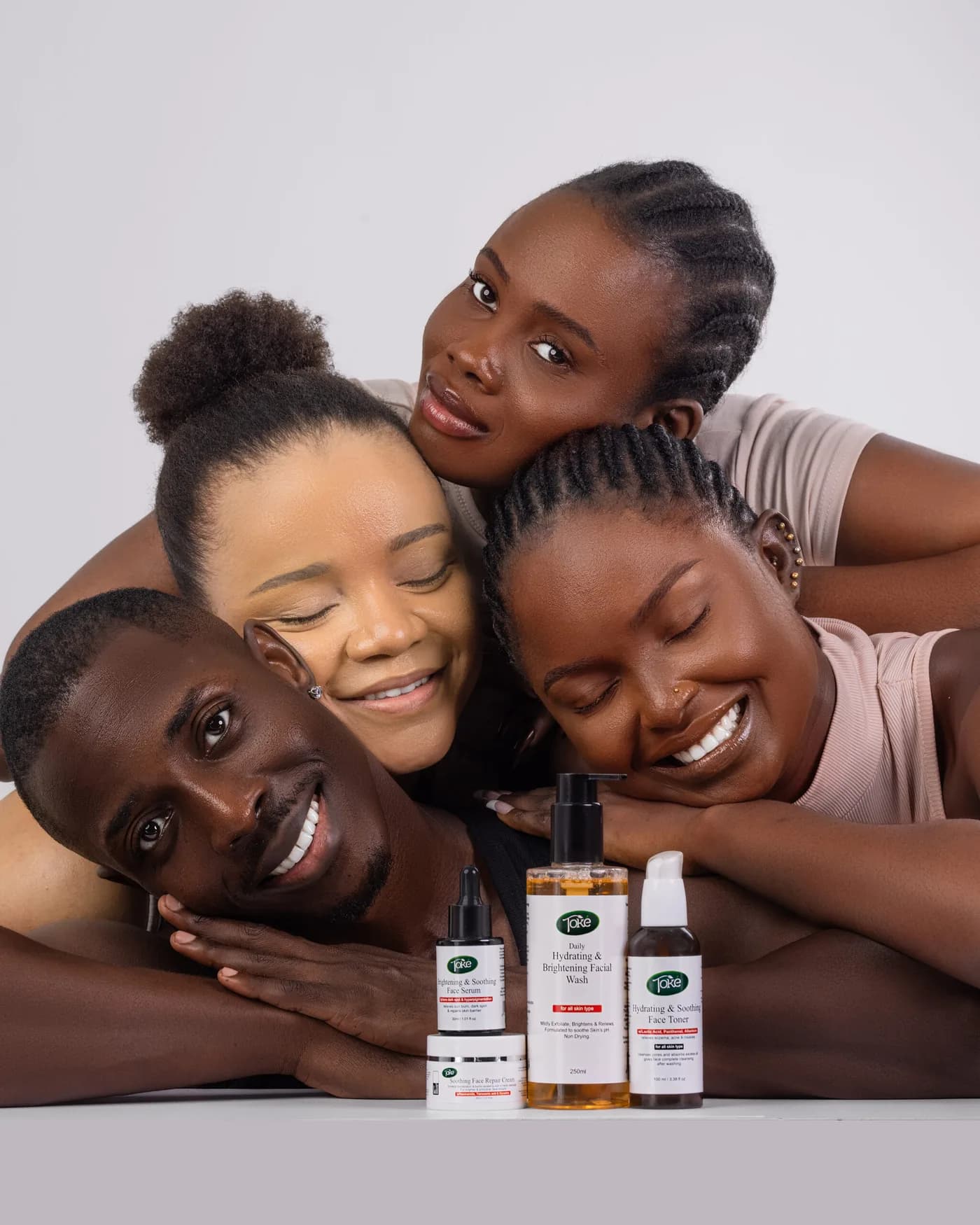 Four people resting their heads together, smiling, with Toke Cosmetics face care products in front of them